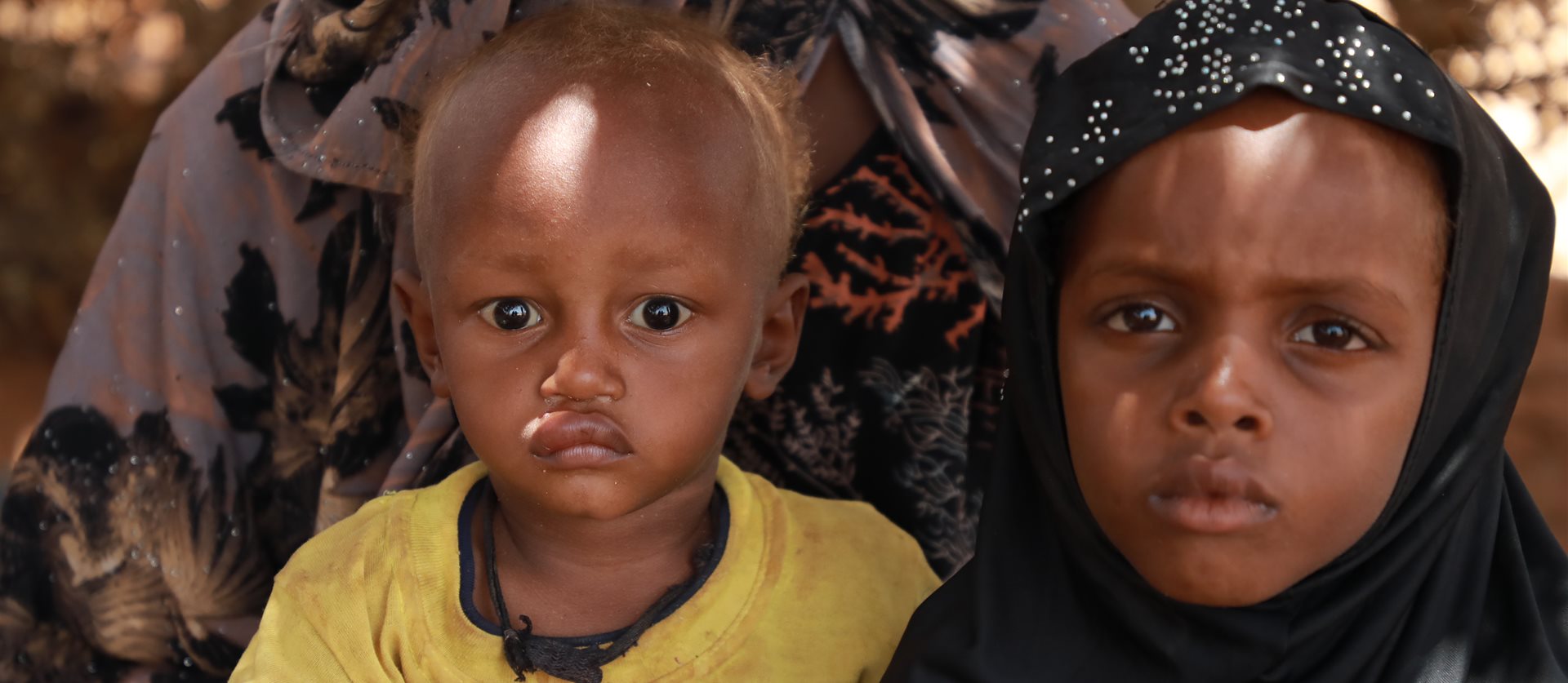 A toddler in a yellow shirt and a girl in a black headscarf